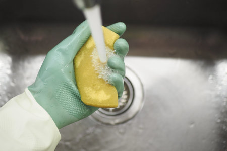 Cleaning sponge under running water in a kitchen sink