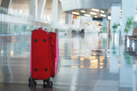 Bright red suitcase stands alone in a modern airport terminalの写真素材