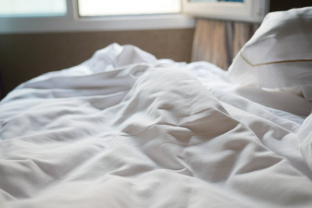 Soft, crumpled sheets on a cozy bed in a sunlit roomの写真素材