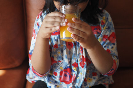 Kid enjoys fresh juice while sitting on a couchの写真素材