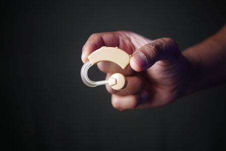 A Hand Holding a Hearing Aid Device for Improved and Enhanced Auditory Assistance Needsの写真素材