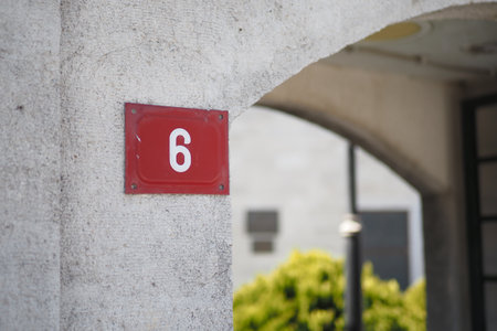 A prominently displayed number 6 sign affixed to a concrete wall, adorned with greeneryの写真素材