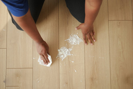 Person cleaning spilled substance from wooden floor in daylightの写真素材