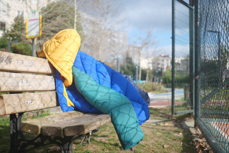 Colorful quilted jacket draped over a park bench on a sunny dayの写真素材