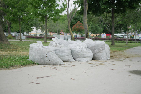 In a vibrant city park, numerous piles of white compost bags are scattered throughoutの写真素材