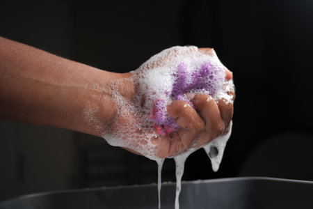 Hand washing a soapy sponge over a container of waterの写真素材