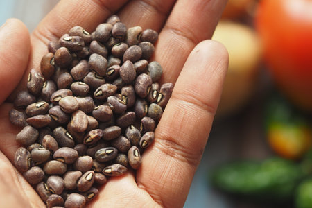 Hand holding raw brown seeds with vegetables in the background