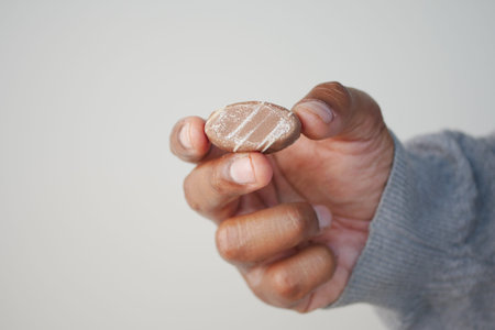 Hand holding a small, oval-shaped candy with stripes indoors