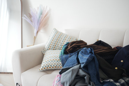 Piles of clothes on a couch in a cozy living room spaceの写真素材