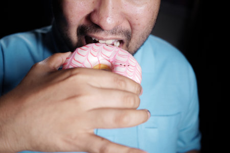 Man enjoying a pink frosted donut at a cozy settingの写真素材