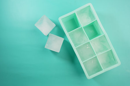 Ice cubes arranged neatly in a green ice tray on a flat surfaceの写真素材
