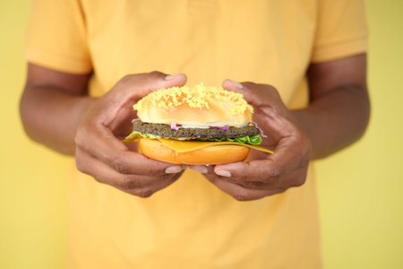 Hand holding colorful burger against a bright yellow backgroundの写真素材