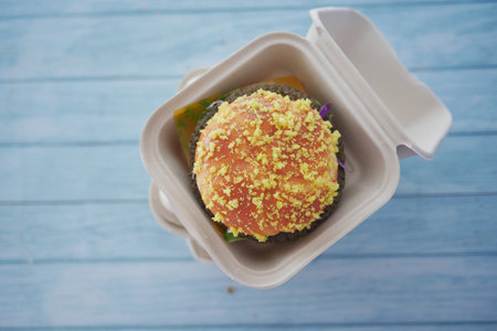 Delicious burger topped with golden cheese in a takeout containerの写真素材