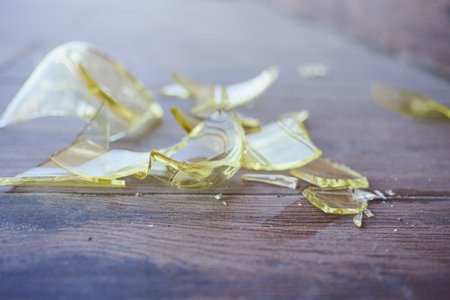Broken yellow glass shards scattered on wooden surface