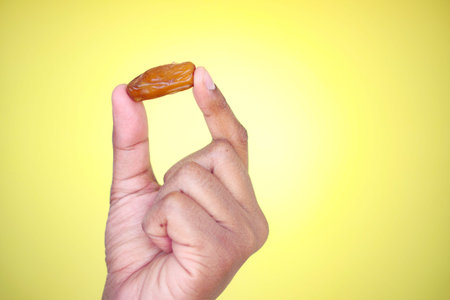 Person holding a date fruit against a vibrant yellow backdrop