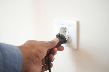Hand inserting electrical plug into wall outlet at home