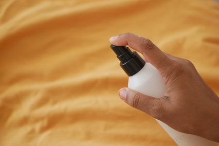 Hand holding a spray bottle above a yellow fabric surfaceの写真素材