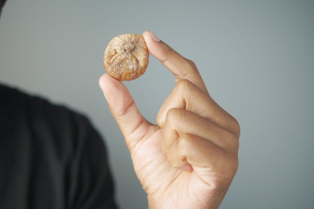 Holding a dried fig in hand against a plain backgroundの写真素材