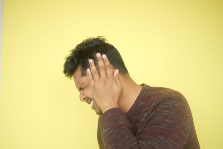 Man with discomfort holding his head by a yellow wall