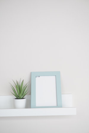Simple decor with a plant and a blank picture frame on a shelfの写真素材