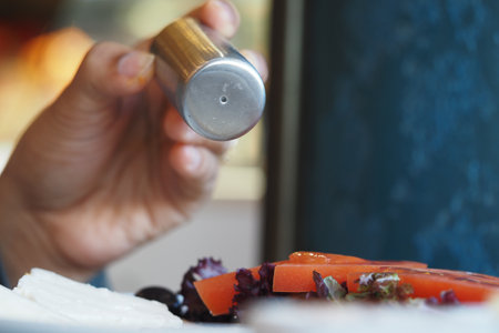 A hand sprinkling salt over a colorful salad in a restaurantの写真素材