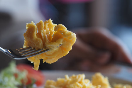 Scrambled eggs on a fork close to a fresh breakfast plateの写真素材