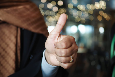 Hand giving a thumbs up with blurred festive lights in the background