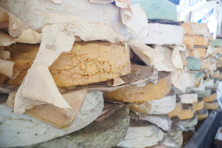 Cheese wheels stacked in an outdoor market during a sunny day