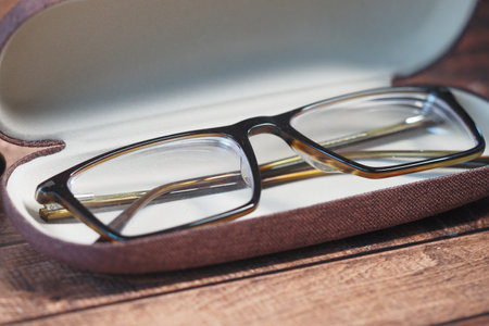 Stylish brown eyeglasses resting in a protective case on a tableの写真素材