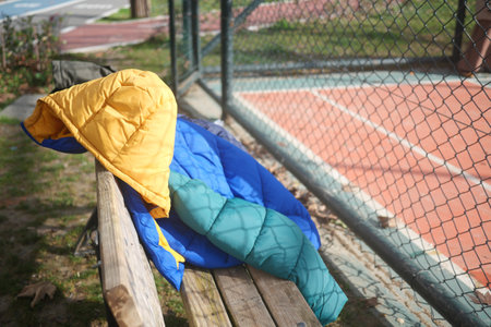 Colorful jacket rests on a wooden bench by the tennis courtの写真素材