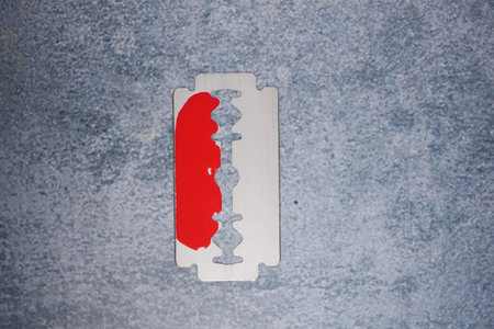 Red paint on metal razor blade on gray surfaceの写真素材
