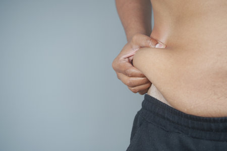 Person pinching abdomen to assess body fat levels in private settingの写真素材