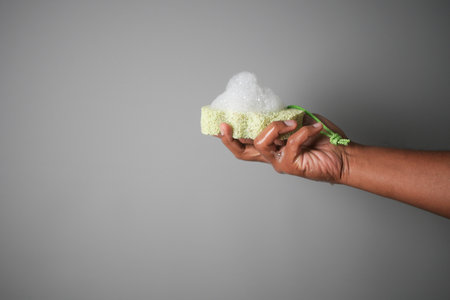Hand holding a soapy cleaning sponge against a gray backgroundの写真素材
