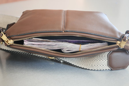 Brown bag with cash peeking out on a table surfaceの写真素材
