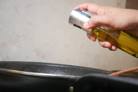 Hand pouring oil into skillet while preparing a meal in the kitchenの写真素材