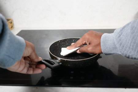 Cleaning a frying pan on an induction cooktop in a kitchenの写真素材