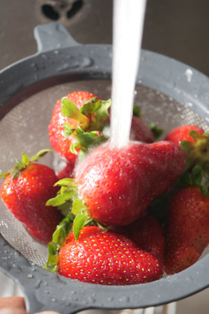 Fresh strawberries being rinsed in a colander under running waterの写真素材
