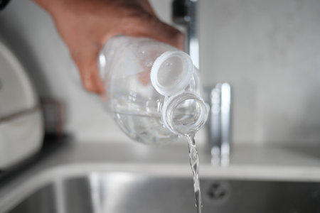 Pouring clear water from a plastic bottle into a kitchen sinkの写真素材