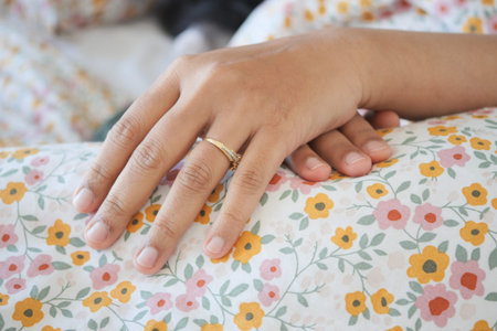 Hand resting on floral bedding with a ring in soft morning light