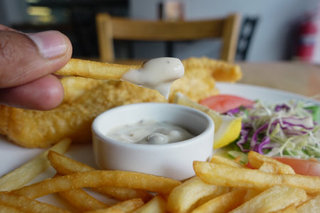 Enjoying crispy fries dipped in creamy sauce at a casual dining spotの写真素材