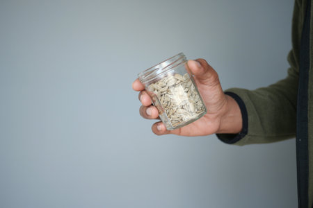 Hand holding a jar filled with seeds against a light backgroundの写真素材