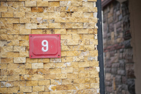 House number nine on a textured yellow wall by a stone buildingの写真素材