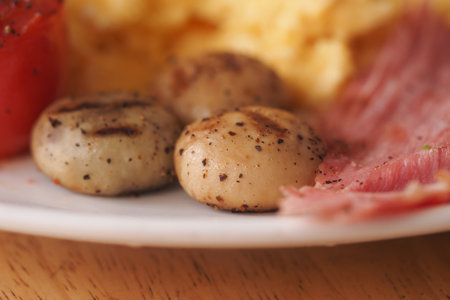 Grilled mushrooms with ham and scrambled eggs on a white plateの写真素材