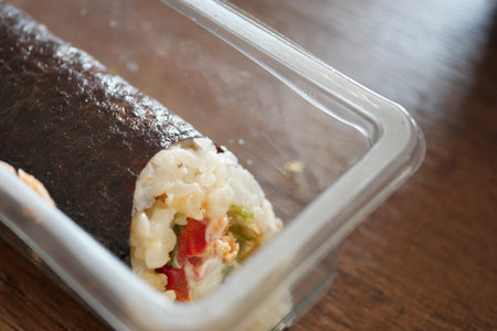 Delicious sushi roll served in a clear container on a wooden tableの写真素材