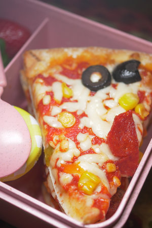 pizza slice with toppings in a pink lunchbox settingの写真素材