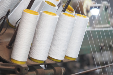 Spools of white thread arranged on a textile machine in a workshopの写真素材