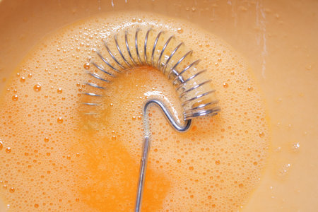 Mixing eggs for a recipe with a whisk in a bowlの写真素材