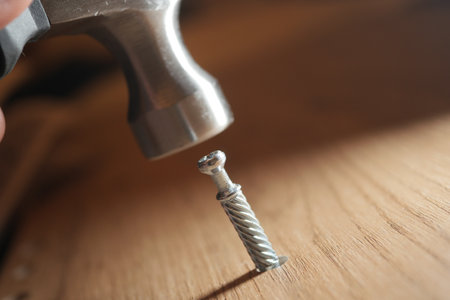 Hammer strikes a screw on a wooden surface during assemblyの写真素材