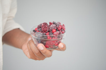Hand holding a bowl of mixed frozen berries with a neutral backgroundの写真素材
