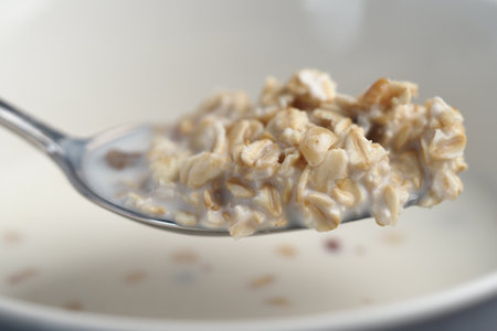Spoon holding creamy oatmeal with milk and grains in close-upの写真素材
